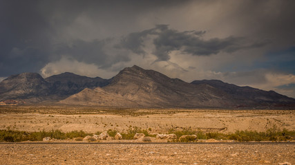Fototapeta na wymiar Nevada Desert and Mountain Range - with a Thin Strip of Road in the Foreground, and a Long Stretch of Flat Land and Brush on a Cloudy, Overcast Day