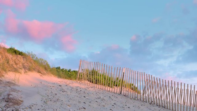 Beautiful shot of dune fence, sand, red clouds, and blue skies at sunset. Camera pans left.