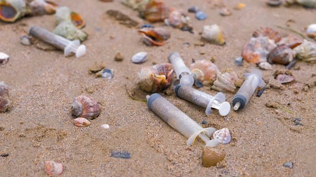 Medical syringes among the rapan shells in sand on sea beach after storm.