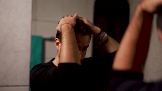Male messing with hair looking in bathroom mirror reflection.