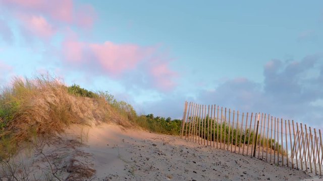 Nice footage sand dunes fence, sand, red clouds, and blue skies at sunset.