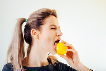 An attractive girl holds a lemon in her hand and licks it with a squint of sour taste.