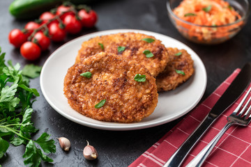 Cutlets lie on a white plate. Chicken cutlets lie among the vegetables on a black stone table.