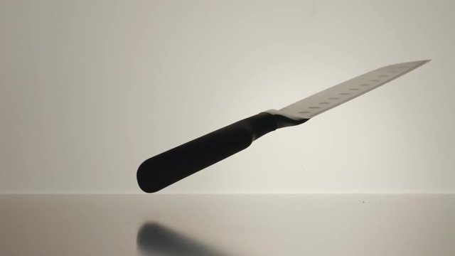 SLOW MOTION: Black cooking knife twisting on the white surface