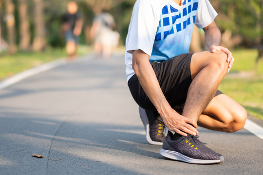 Young fitness man holding his sports leg injury. muscle painful during training. Asian runner having ankle ache and problem after running and exercise outside morning. sport and healthy concepts
