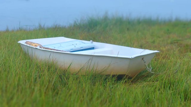 Little blue dinghy rowboat beached in dune grass wetlands at low tide.