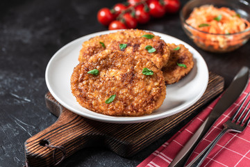 Cutlets lie on a white plate. Chicken cutlets lie among the vegetables on a black stone table.