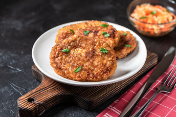 Cutlets lie on a white plate. Chicken cutlets lie among the vegetables on a black stone table.