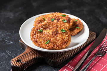 Cutlets lie on a white plate. Chicken cutlets lie among the vegetables on a black stone table.