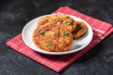 Cutlets lie on a white plate. Chicken cutlets lie among the vegetables on a black stone table.