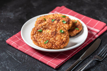 Cutlets lie on a white plate. Chicken cutlets lie among the vegetables on a black stone table.