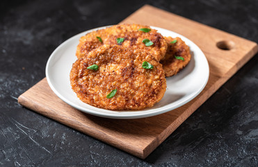 Cutlets lie on a white plate. Chicken cutlets lie among the vegetables on a black stone table.