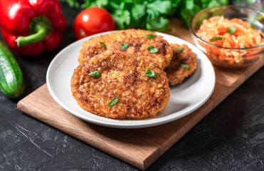 Cutlets lie on a white plate. Chicken cutlets lie among the vegetables on a black stone table.