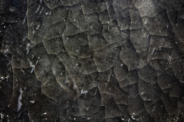 Top view of cracked ice surface darkened for a dramatic look, with snow on edges of the frame.