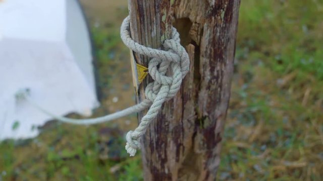 Knot tied around a wooden pole - camera pans to little dinghy rowboat beached in dune grass wetlands at low tide.