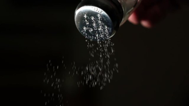 Salt falling in super slow motion from a salt shaker against black background 