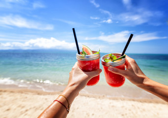 Fresh watermelon juice with a straw in two glasses against a bright tropical landscape, against the...