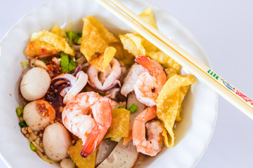 Seafood noodle Tom Yum in white bowl on white background, Thai food, Street food..Egg noodles served “dry” with seafood.