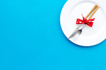 Dating on Valentine's day concept. Festive dishes, tableware on plate on blue background top view copy space