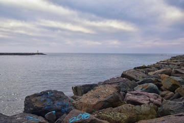 View from Mission Beach in San Diego, of Piers, Jetty and sand, around surfers, including warning signs, palm trees, waves, rocks, boats and horizon views. Pacific Ocean. California, United States.