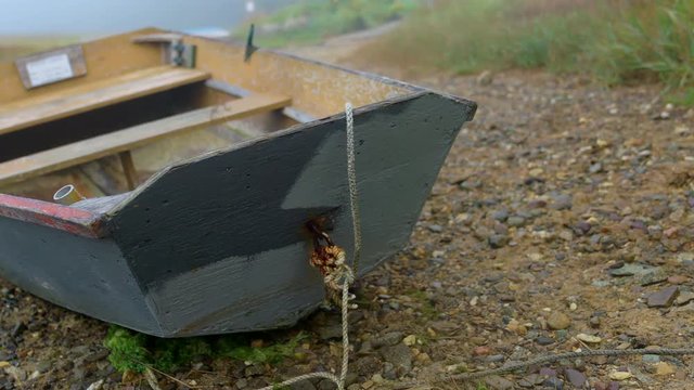 Nice shot of rustic wooden rowboat dinghy beached on rocky shore. Camera pans left.