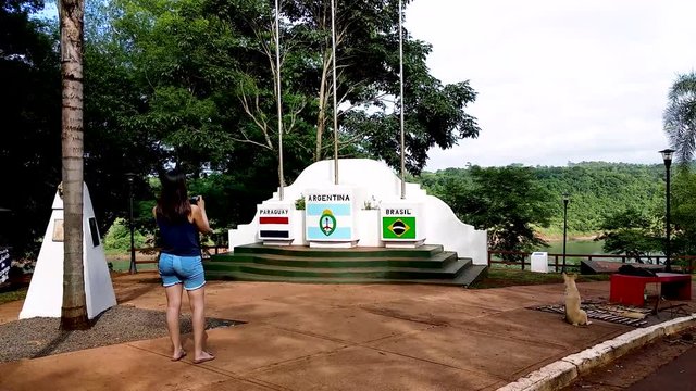 POV walking up behind female taking photo on smartphone, Argentine tres frontere monument.