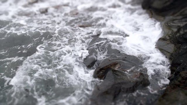 Dramatic slow-motion ocean wave rolling onto rocky shore.  Dark and ominous.