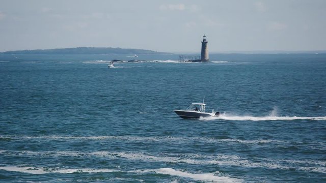 Motorboat passing the Ram Island Ledge Light Station in Casco Bay near Portland, Maine on a nice summer day with blue water - slow motion