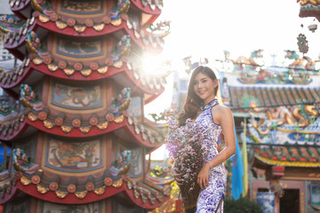 Portrait of Chinese woman wear traditional dress cheongsam and holding flower bouquet at chinese shrine in chinese new year, China Girl.