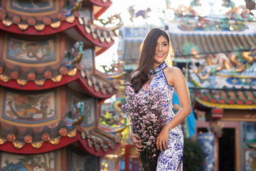 Portrait of Chinese woman wear traditional dress cheongsam and holding flower bouquet at chinese shrine in chinese new year, China Girl.