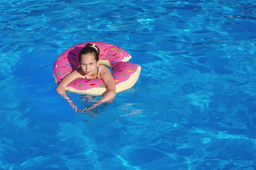 Girl teenager in a swimsuit swims with an inflatable ring in the pool with blue water.