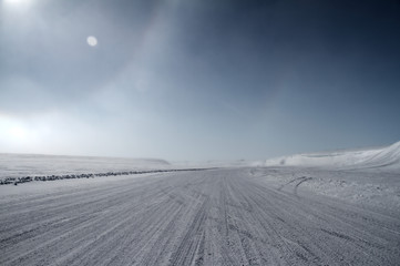 An ice road leading towards snow covered hills with a partial sundog located near the community of Cambridge Bay, Nunavut, Canada