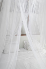 Bed with white linen, pillows and mosquito net. Vintage Interiors. Bed with canopy net.