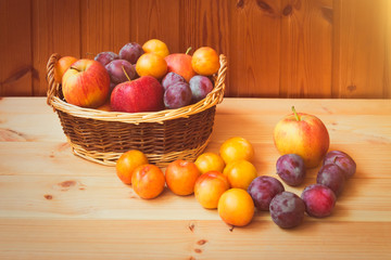 Wicker basket with apples and colorful plums on wooden table. Selective focus.