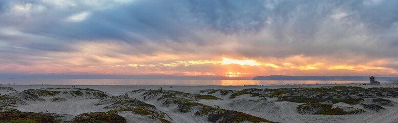 Coronado Beach in San Diego by the Historic Hotel del Coronado, at sunset with unique beach sand dunes, panorama view of the Pacific Ocean, silhouettes of people walking and boats in California, Unite