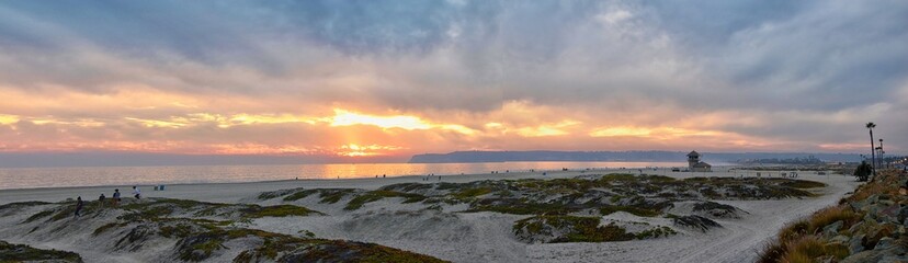 Coronado Beach in San Diego by the Historic Hotel del Coronado, at sunset with unique beach sand dunes, panorama view of the Pacific Ocean, silhouettes of people walking and boats in California, Unite