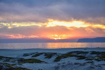 Coronado Beach in San Diego by the Historic Hotel del Coronado, at sunset with unique beach sand dunes, panorama view of the Pacific Ocean, silhouettes of people walking and boats in California, Unite