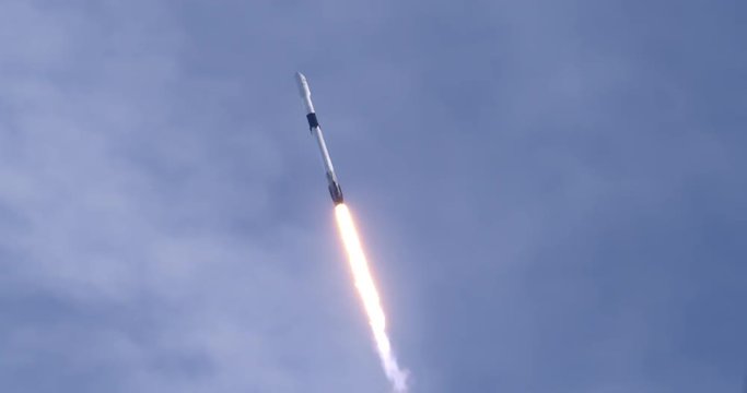 Rocket launching into space through blue skies and clouds. Flames and smoke trail behind the rocket. 4K video at 120 fps slow motion. With audio.