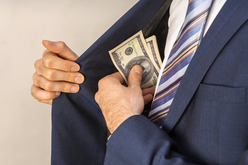 A man in an expensive suit puts money in the inside pocket of his jacket. Concept on the topic of corruption.