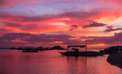 Fototapeta na wymiar Sunset on a beach in the Philippines, with overhanging palm trees, and floating boats. Blue hour capture, with orange and mauve sky