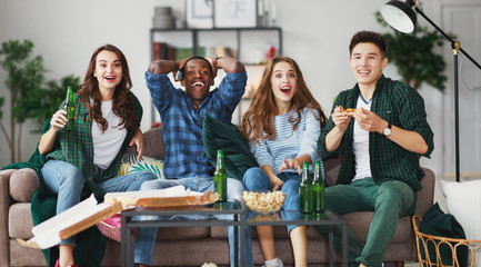 group of happy friends fans watching a match on tv with beer and pizza at home.