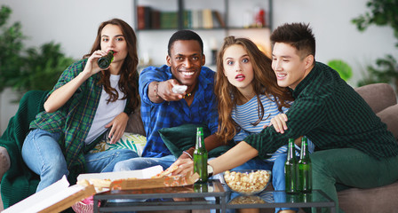 group of happy friends fans watching a match on tv with beer and pizza at home.