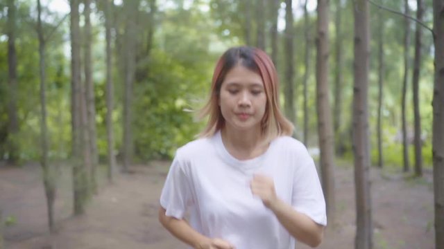 Slow motion - Healthy beautiful young athletic sporty Asian runner woman in sports clothing running and jogging on forest trail. Lifestyle fit and active women exercise in the forest concept.