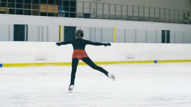 Panning shot of young figure skating girl sliding on ice, jumping and falling down on ice rink