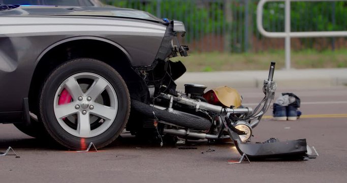 Damaged motorcycle is wedged under the front bumper of a car after a fatal traffic accident where the motorcyclist was killed in the crash.