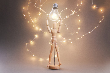 A wooden man holding a glowing bulb over his head. The symbol of the idea.
