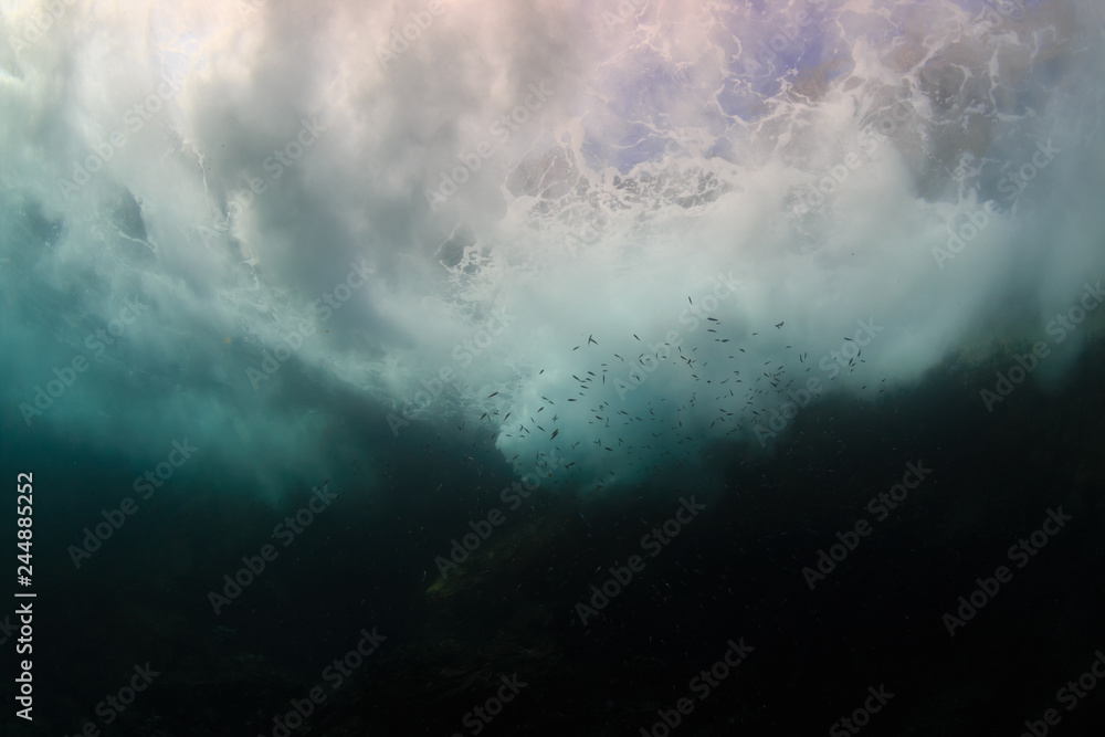 Wall mural Underwater view of waves crashing against rocks producing bubbles, foam and spray