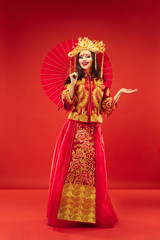 Chinese traditional graceful woman at studio over red background. Beautiful girl wearing national costume. Chinese New Year, elegance, grace, performer, performance, dance, actress, emotions concept