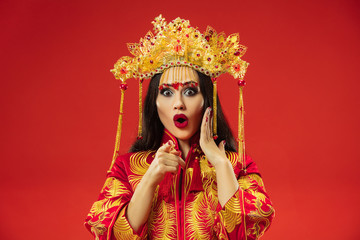 Chinese traditional graceful woman at studio over red background. Beautiful girl wearing national costume. Chinese New Year, elegance, grace, performer, performance, dance, actress, emotions concept