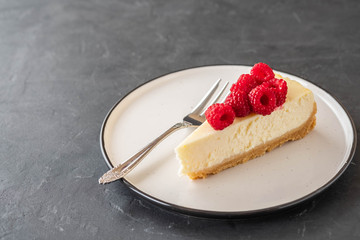 Slice of New York Cheesecake with raspberries on a dark background.